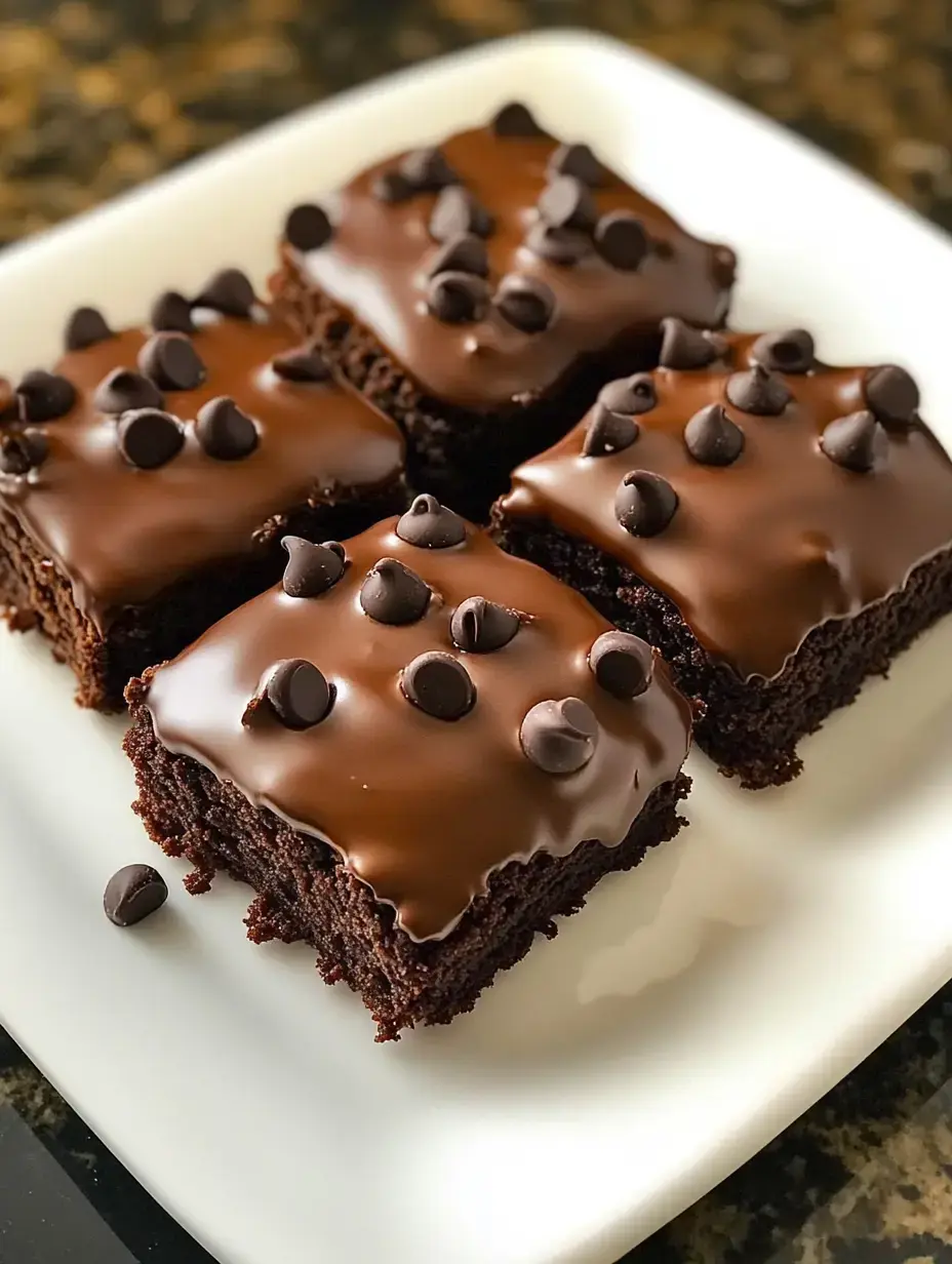 Um prato de brownies de chocolate cobertos com cobertura brilhante de chocolate e salpicados com gotas de chocolate.